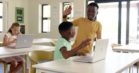 Diverse Teen Students High-Fiving While Collaborating on Laptops in Bright Classroom