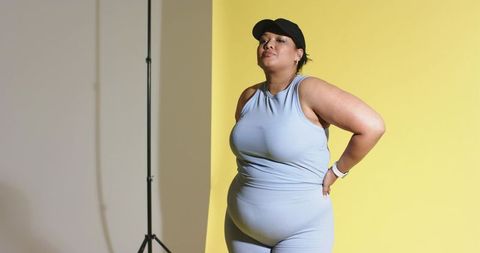 Confident curvy woman standing and posing in blue ribbed activewear on yellow backdrop