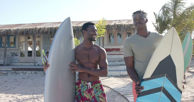 Happy diverse friends with surfboards talking over beach house. Vacation, free time, summer and friendship.