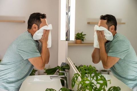 Mature asian man washing face at modern bathroom vanity with plants and mirror reflection