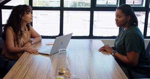 African american women collaborating on performance review at boardroom table with laptop
