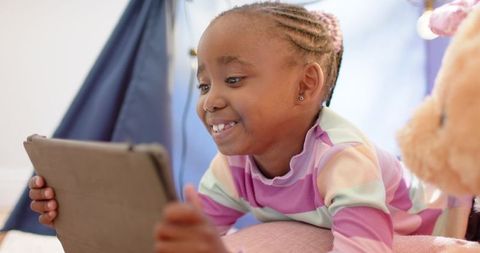African american girl smiling while using tablet in cozy teepee playroom