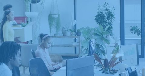 Young professionals typing and collaborating in bright plant-filled open-plan workspace