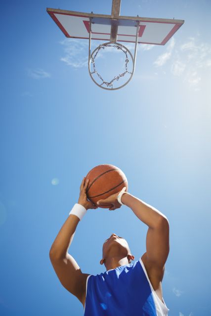 Directly below shot of teenage boy playing basketball against sky on sunny day