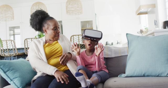 Mother and daughter enjoying virtual reality experience at home. Mother watching lovingly while child explores VR world with excitement. Perfect for use in technology, family, or home lifestyle articles. Ideal for concepts of modern parenting, recreational technology use in families, and familial bonding activities.