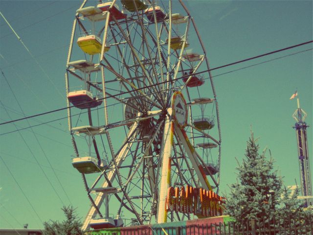 Classic ferris wheel at fairground with clear sky in vintage style. Perfect for themes involving amusement parks, fairs, leisure activities, family entertainment, outdoor fun, nostalgic scenes, and retro aesthetics. Ideal for promotional materials, travel brochures, and vintage-themed designs.
