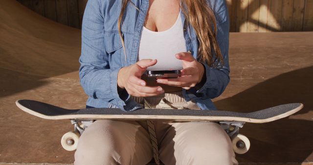 Image of midsection of caucasian female skateboarder resting and using smartphone. Skateboarding, sport, active lifestyle and hobby concept.