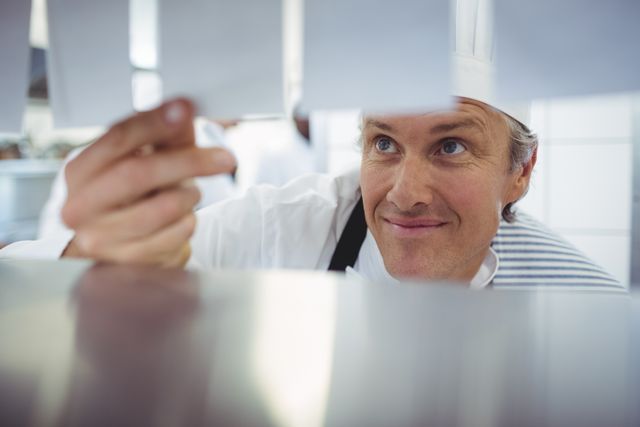 Smiling Chef Checking Order List in Commercial Kitchen - Download Free Stock Photos Pikwizard.com