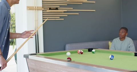 Diverse friends playing pool in modern lounge, lining up cue shot on green felt table