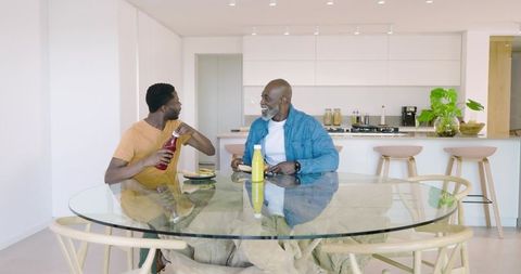 Father and Son Sharing Meal at Glass Dining Table in Modern Kitchen