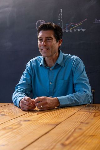 Man in Blue Shirt Engaging in Classroom Discussion Near Graph Chalkboard
