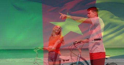 Laughing couple cycling on sunny beach with cameroon flag overlay for summer travel and fun