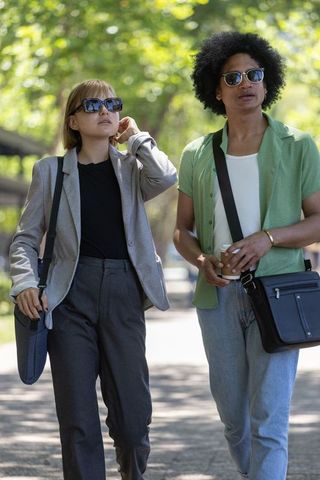 Diverse colleagues walking through sunlit park wearing business casual and sunglasses