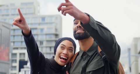 Joyful couple pointing at urban landmark in city
