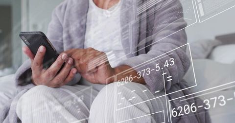 Senior woman tapping smartphone while wearing gray robe with digital interface overlay