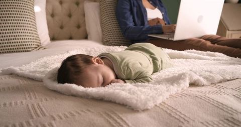 Working mother balancing remote work and caring for sleeping baby