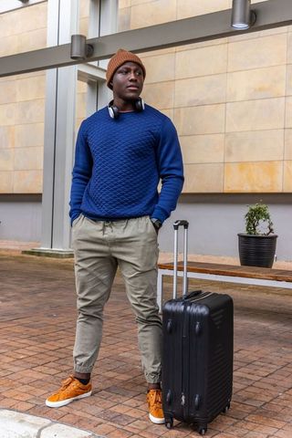 African american traveler standing with luggage and headphones at urban transit entrance