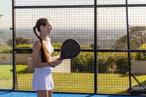 Female player enjoying padel match on sunny outdoor court with scenic view