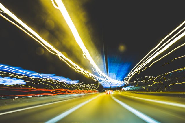 Long exposure showing colorful light trails on busy highway at night, creating abstract patterns. Useful as a background for products related to speed, travel, urban life, or futuristic themes. Ideal for marketing materials, website headers, or presentations.
