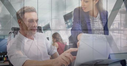 Mature businessman collaborating with female colleague on tablet in modern glass office