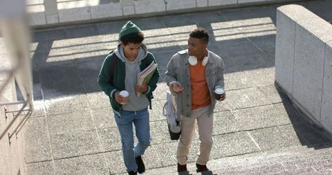 College students walking up urban stairs carrying coffee, backpacks and notebooks