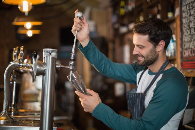 Bartender pouring beer from tap into glass while smiling. Ideal for use in advertisements for bars, pubs, and restaurants, as well as promotional materials for hospitality services and nightlife events.