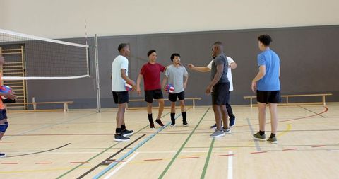 Multicultural male volleyball team collaborating during indoor practice on gym court holding balls