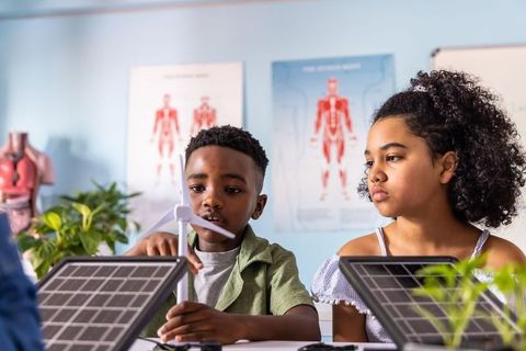 Black kids building clean energy models in stem class using wind turbine and solar panels