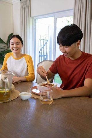 Asian couple enjoying meal with chopsticks at home dining