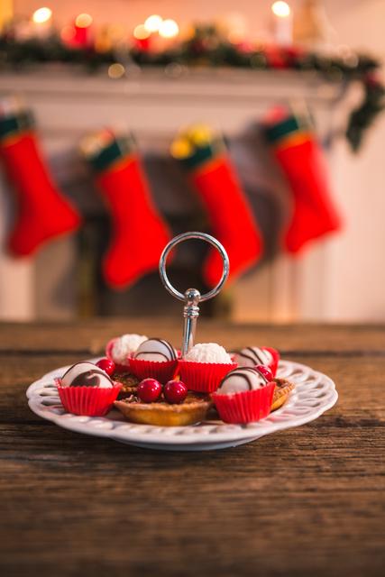 Assorted Christmas desserts arranged on a festive plate with a blurred background featuring red Christmas stockings hanging by a fireplace. Ideal for holiday-themed promotions, festive recipe blogs, and Christmas celebration advertisements.