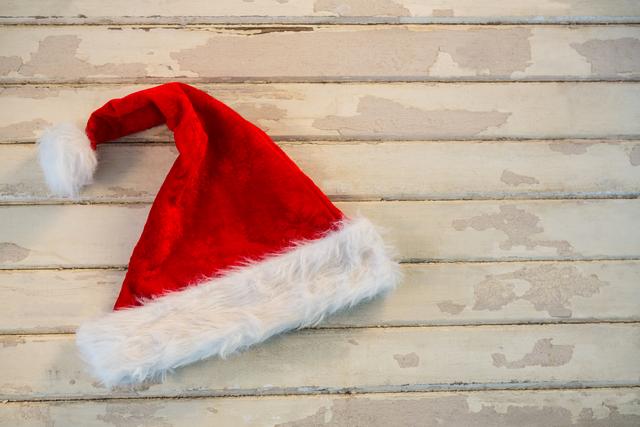 Santa hat lying on rustic wooden plank, evoking a cozy and festive holiday atmosphere. Ideal for Christmas-themed designs, holiday greeting cards, festive advertisements, and seasonal social media posts.