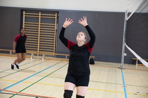 High school volleyball player raising arms preparing overhead pass on indoor gym court