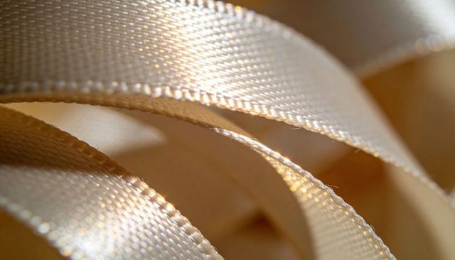 Curling cream satin ribbon revealing woven texture and stitched edges