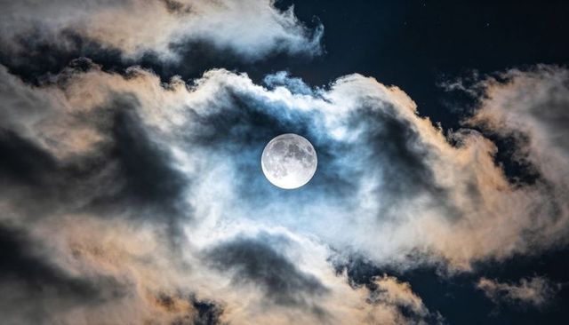 Glowing Full Moon with Halo and Layered Clouds Over Dark Starry Sky, Dramatic Lunar Night