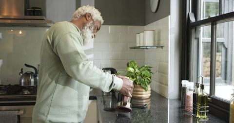 Senior man preparing coffee with french press in modern kitchen
