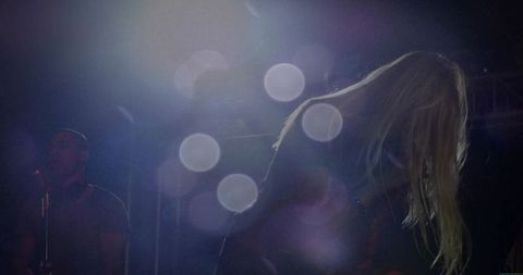 Backlit Female Vocalist Leaning Forward on Moody Concert Stage with Bokeh Light Halos