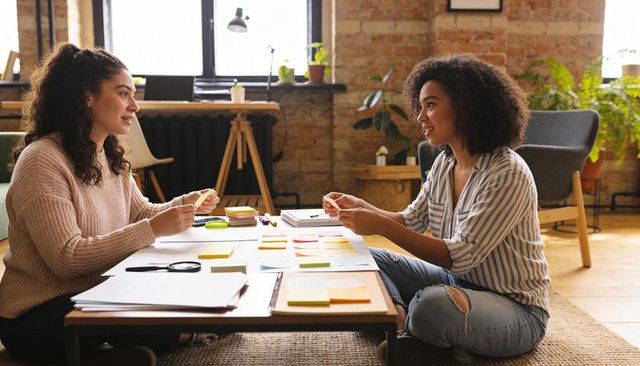 Two women brainstorming with sticky notes in cozy industrial loft workspace for startups