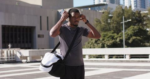 African American Man Adjusting Headphones on Urban Rooftop with Gym Duffel Bag