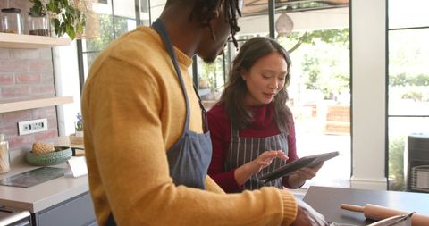 Diverse Couple Baking Together Using Tablet for Recipe Inspiration