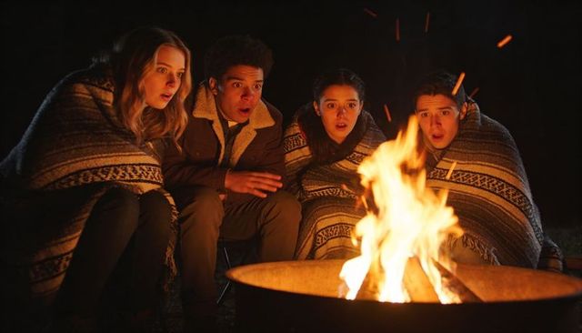 Teenagers gathering around campfire at night wrapped in blankets watching sparks
