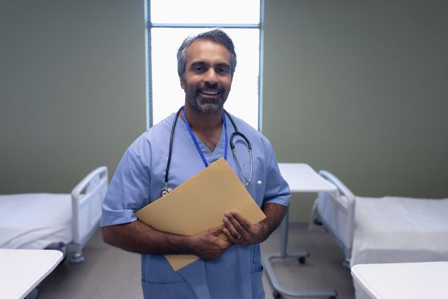 Portrait of biracial male doctor holding medical file in the ward at hospital