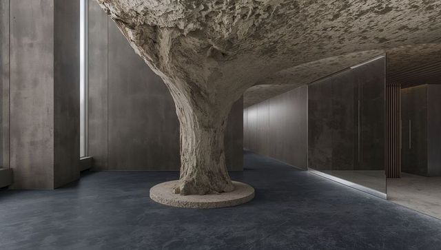 Sculpted concrete column anchoring minimalist lobby with recessed floor lighting
