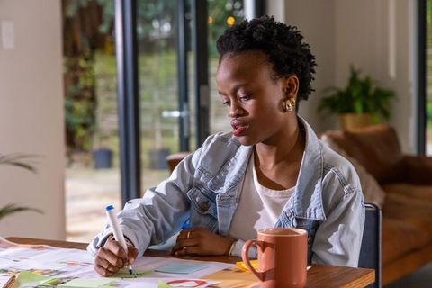 African american woman sketching design concepts in home workspace with coffee mug