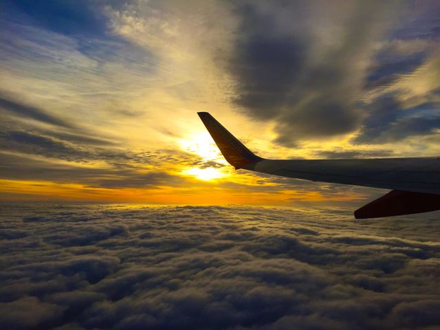 Airplane wing casting shadow over soft clouds colored by golden sunlight from setting sun. Useful for travel advertisements, inspiring adventure blogs, or illustrating concepts of aviation and peaceful journeys.