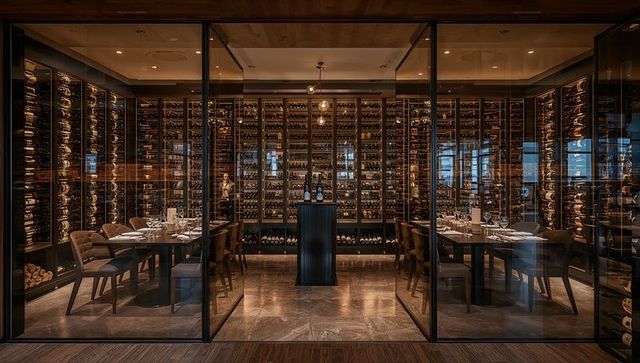 Sommelier arranging bottles in glass-enclosed luxury wine cellar with intimate dining