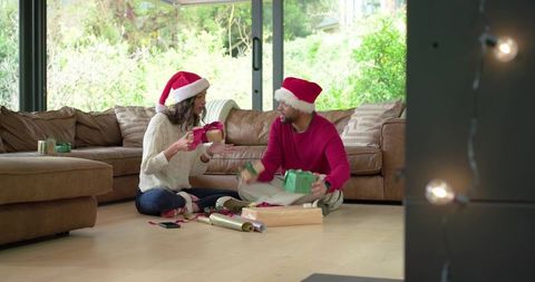 Couple exchanging christmas gifts on living room floor wearing santa hats
