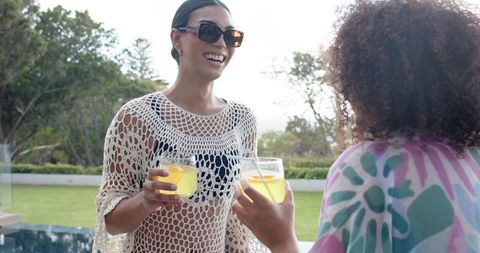 African american women smiling poolside holding citrus drinks wearing crochet coverups
