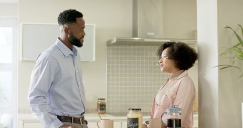 Mid-adult couple having morning conversation over coffee at sunlit modern kitchen counter