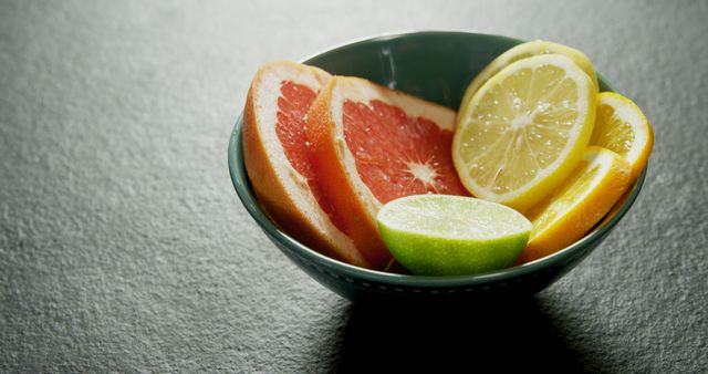 A bowl filled with citrus fruit slices, including grapefruit, lemon, and lime, sits on a textured surface. The vibrant colors of the fruit provide a fresh and healthy visual appeal.