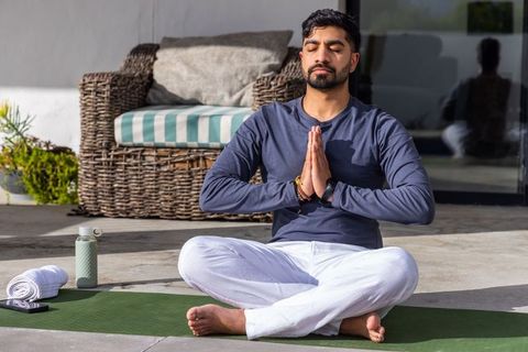 Indian man meditating on patio practicing yoga and mindfulness for wellness and calm
